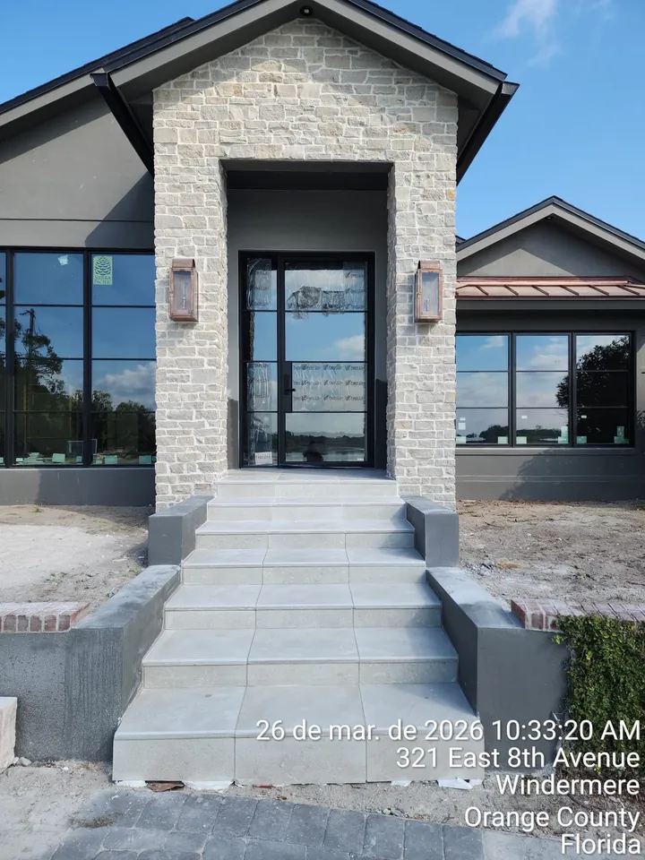 Narrow side-yard patio of square concrete pavers on gravel, open joints, between a house wall and a vinyl fence