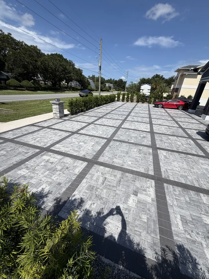 Gray herringbone paver driveway crossed by charcoal banding, running from the curb to a two-car garage