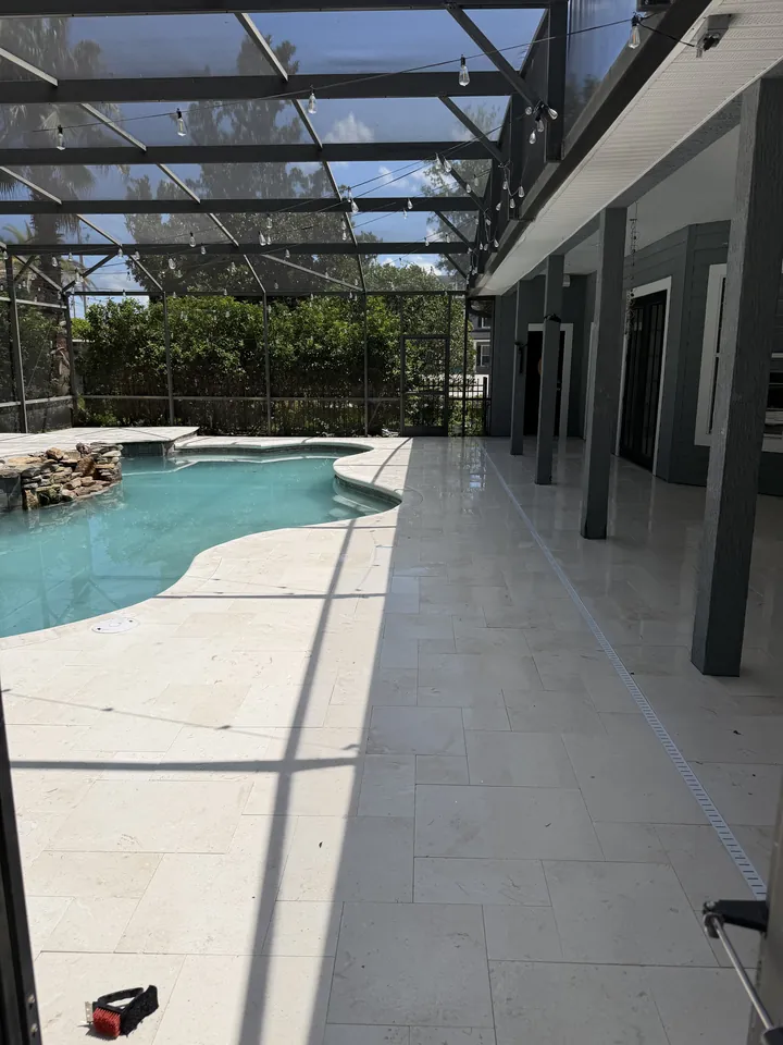 Caged lanai floored in marble pavers around a freeform pool, with a slot drain and a stacked-rock waterfall